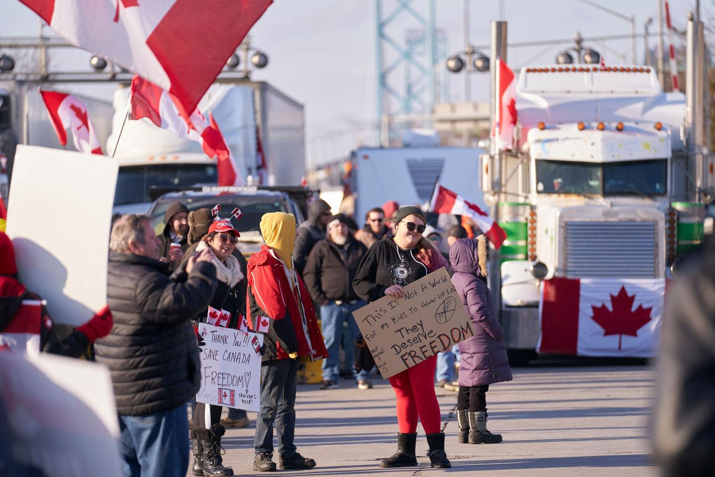 Protesters with signs stand amid trucks and Canadian flags
