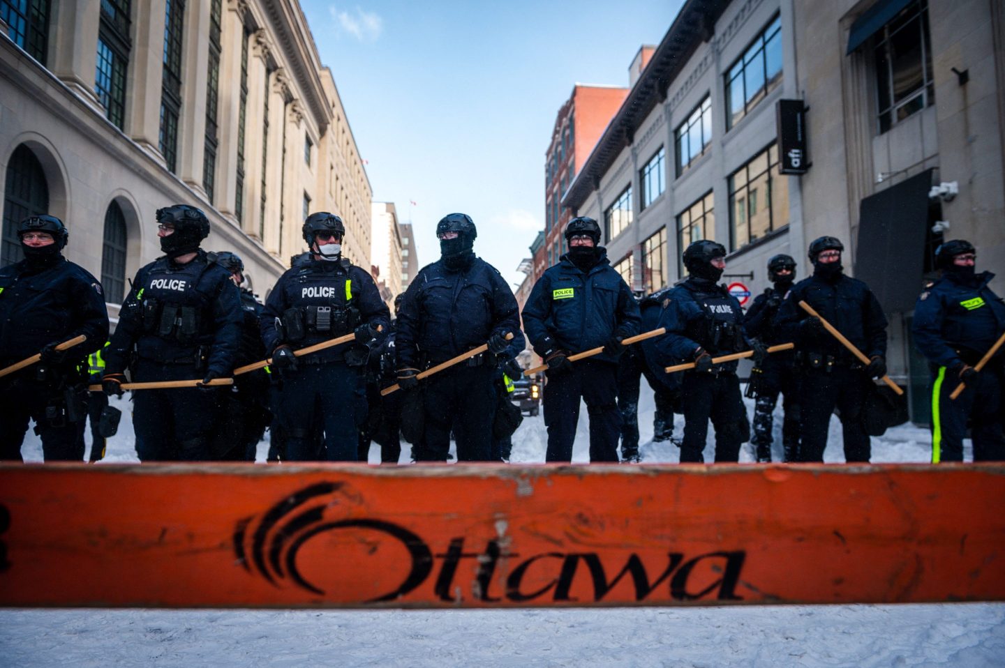 A line of police armed with sticks stand behind a blockade in Ottawa
