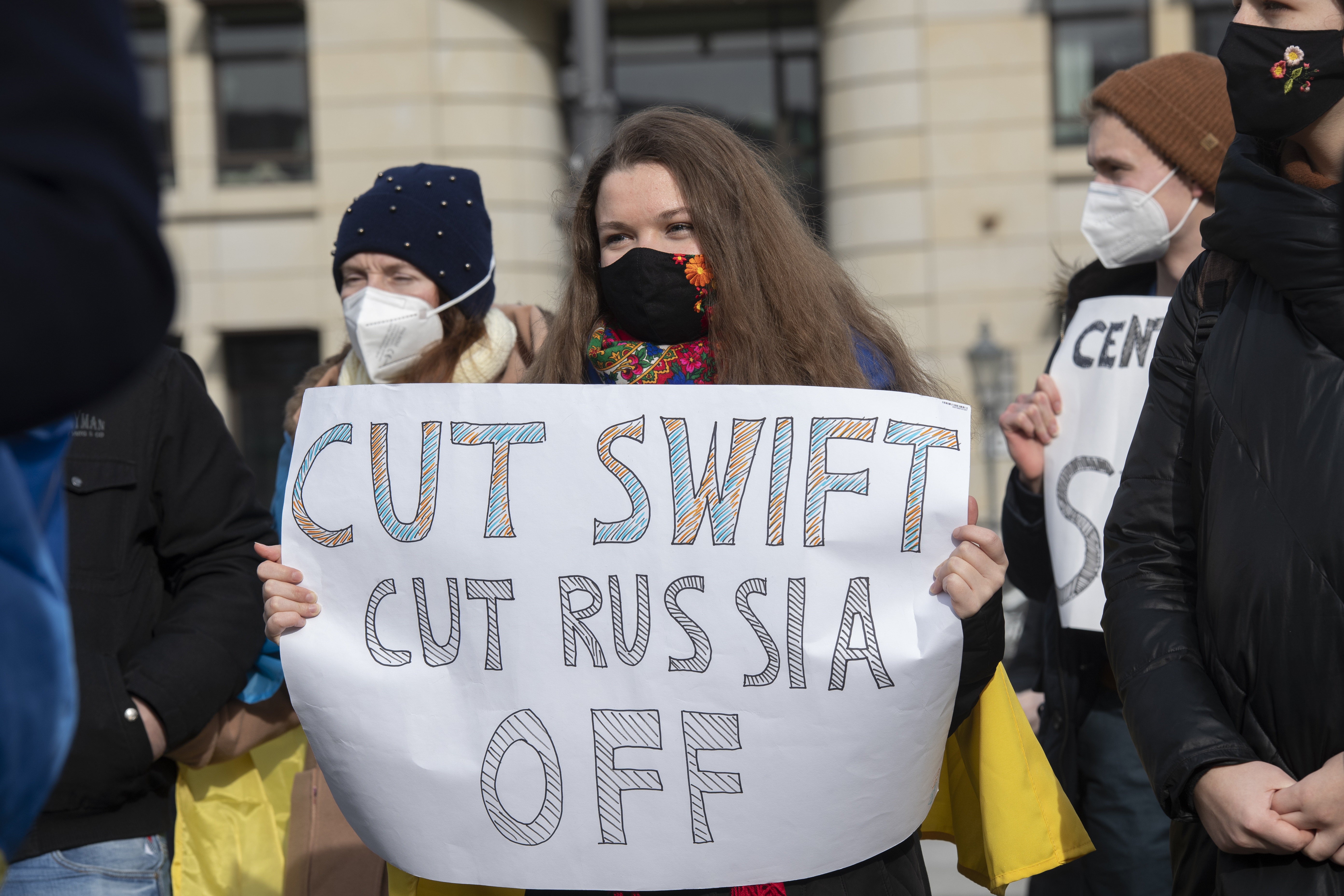24 February 2022, Berlin: Participants in a solidarity demonstration for Ukraine stand in Paris Square with a poster "Cut Swift Cut Russia Off".
