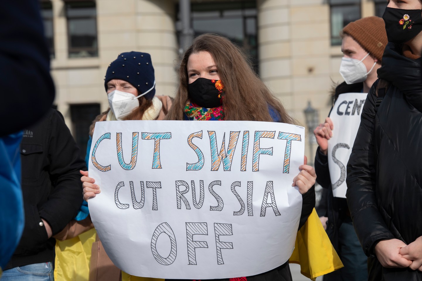 24 February 2022, Berlin: Participants in a solidarity demonstration for Ukraine stand in Paris Square with a poster "Cut Swift Cut Russia Off".