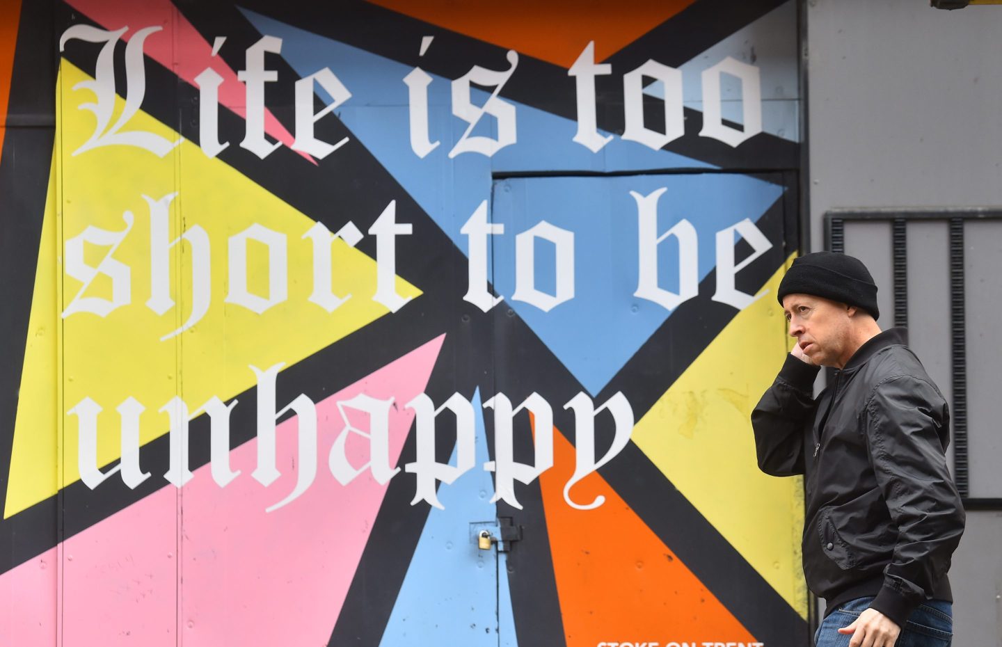 man walking in front of sign that reads "Life is too short to be unhappy".