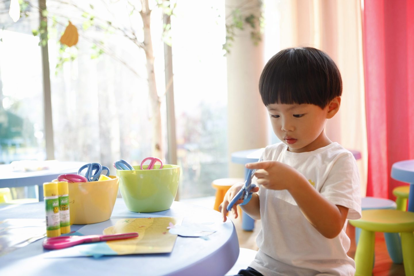 Little Asian boy sitting at a table playing with crafts