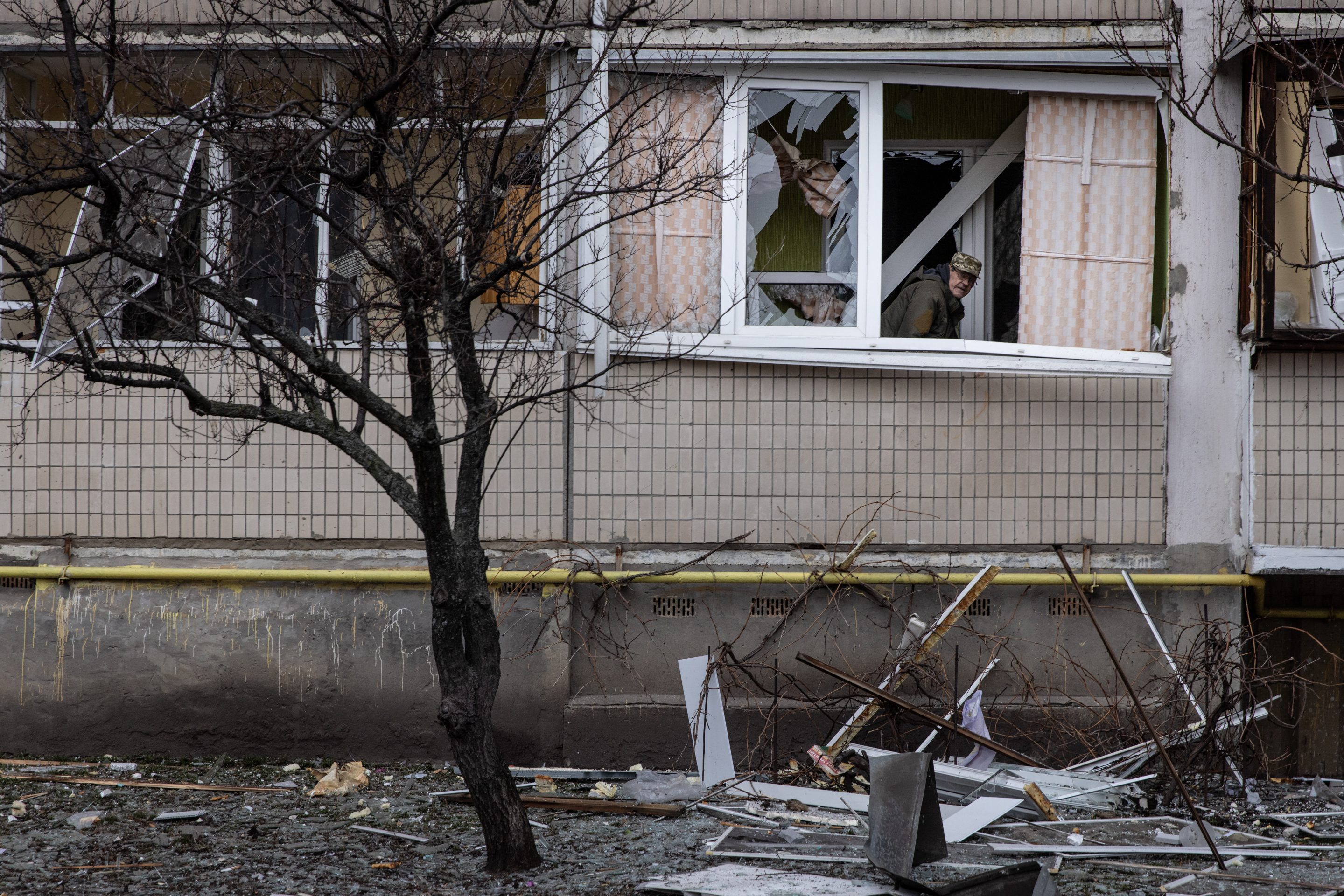 A resident looks out from a damaged window of his apartment in a residential block hit by an early morning missile strike on Kyiv after Russia began a large-scale attack on Ukraine.