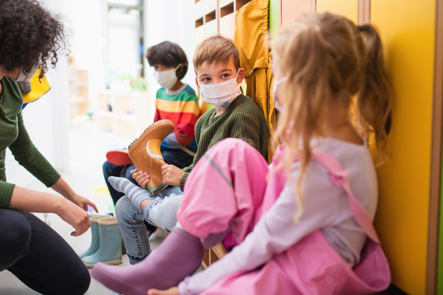 3 preschool children with a teacher near lockers in their classroom