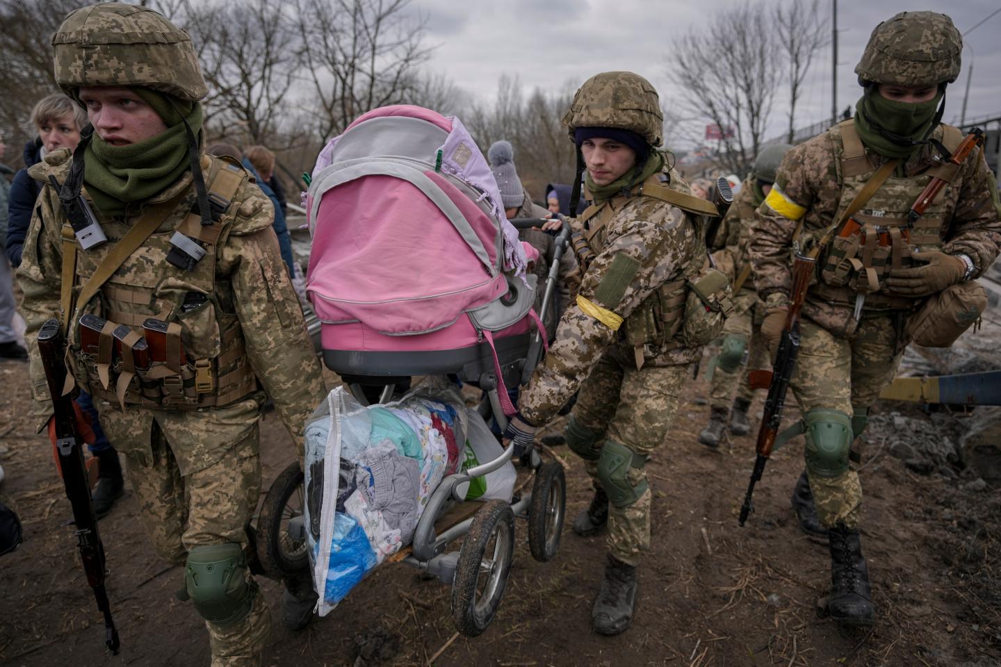 Ukrainian servicemen carry a baby stroller after crossing the Irpin river on an improvised path under a bridge that was destroyed by a Russian airstrike, while assisting people fleeing the town of Irpin, Ukraine, Saturday, March 5, 2022. What looked like a breakthrough cease-fire to evacuate residents from two cities in Ukraine quickly fell apart Saturday as Ukrainian officials said shelling had halted the work to remove civilians hours after Russia announced the deal. (AP Photo/Vadim Ghirda)