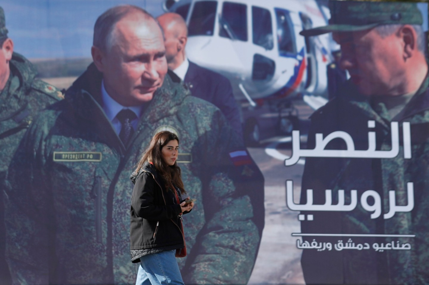 A woman passes a billboard showing Russian President Vladimir Putin in Damascus, Syria, on March 7. The Arabic in poster reads, "The victory for Russia."