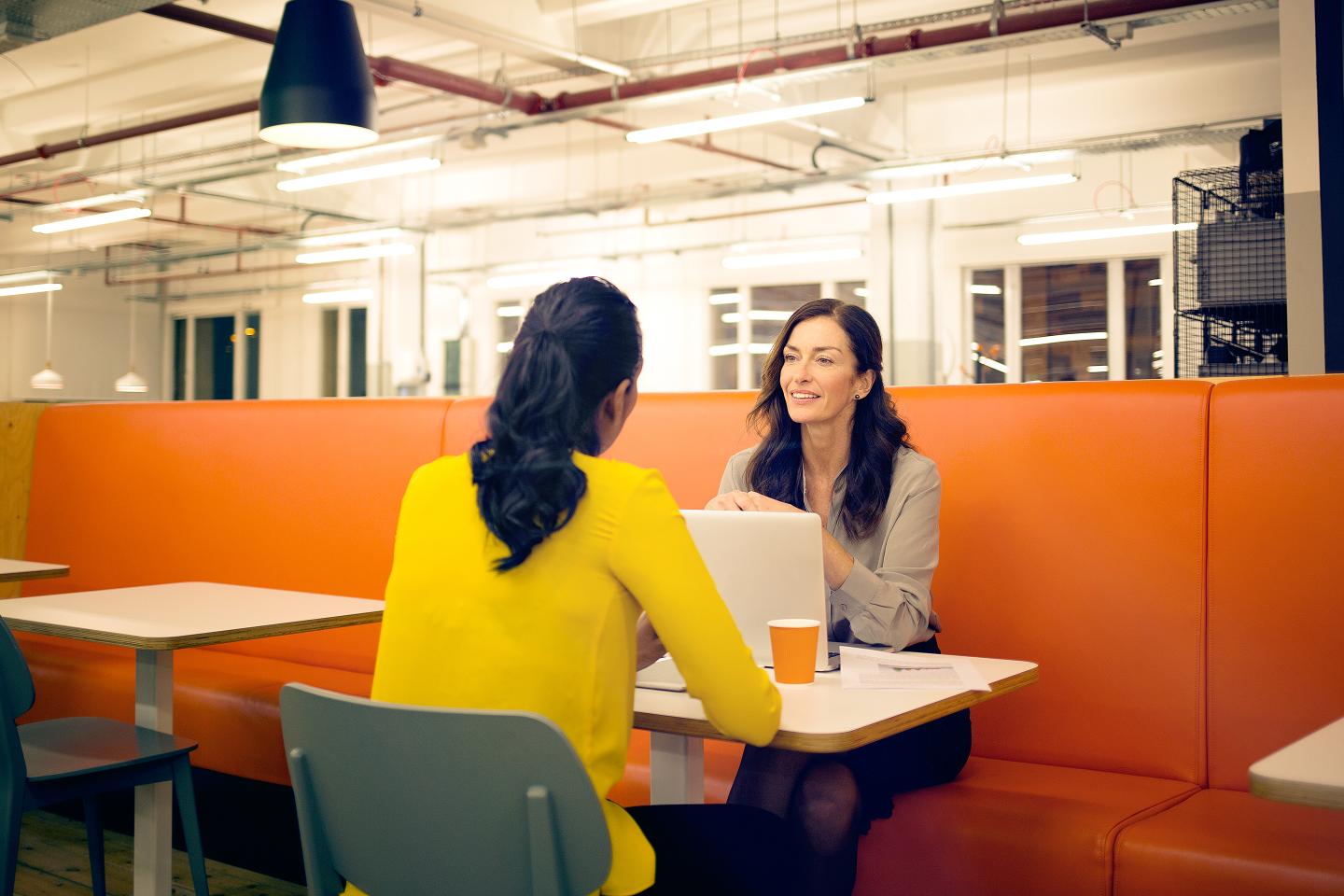 Two women talking at a table in a modern office.