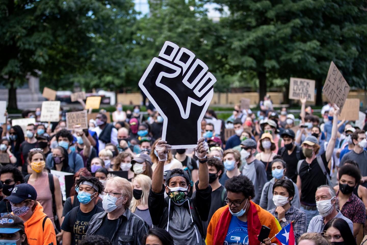 A protester holds a large black power raised fist in the middle of the crowd.