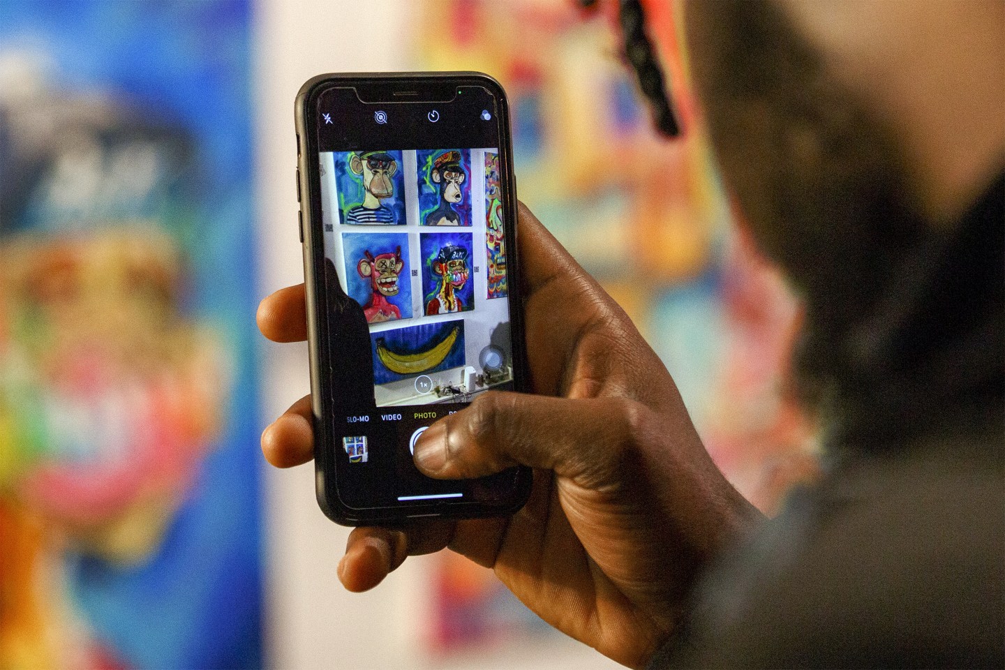 A visitor photographs physical artworks of Bored Ape Yacht Club paintings.