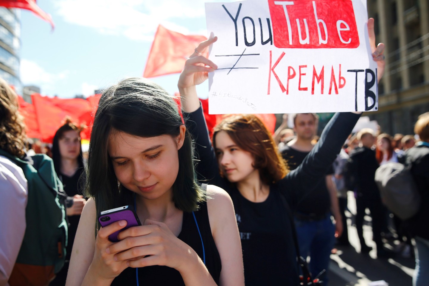 A Russia girl looks at her phone and another holds up a sign at a Russian opposition rally.