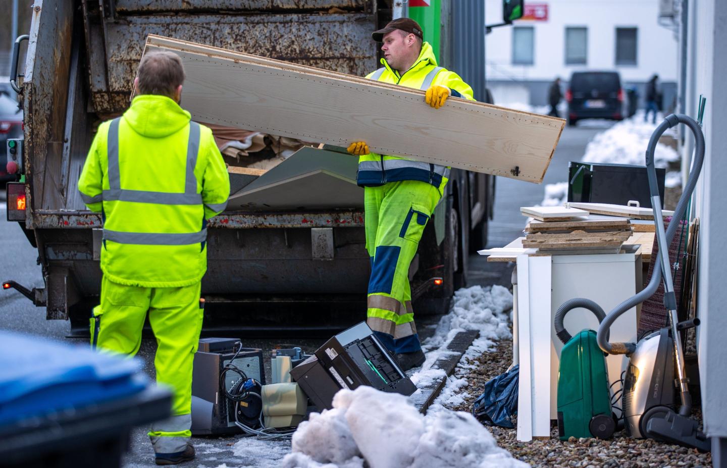 A waste management company throws old furniture boards into a garbage truck.
