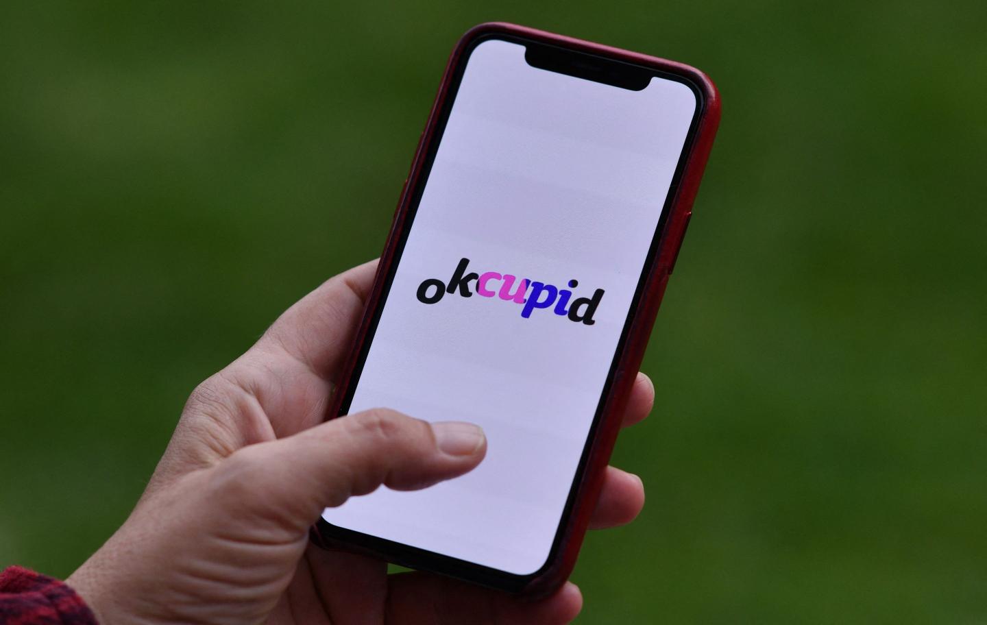 illustration shows a person looking at the OkCupid dating app on a smartphone