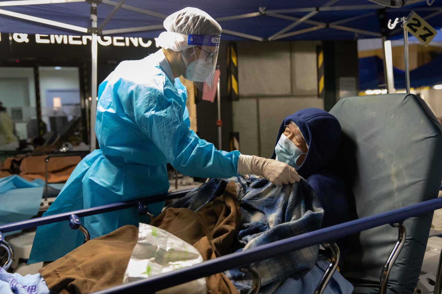 A hospital worker tends to an elderly patient on a hospital bed in a hospital car park