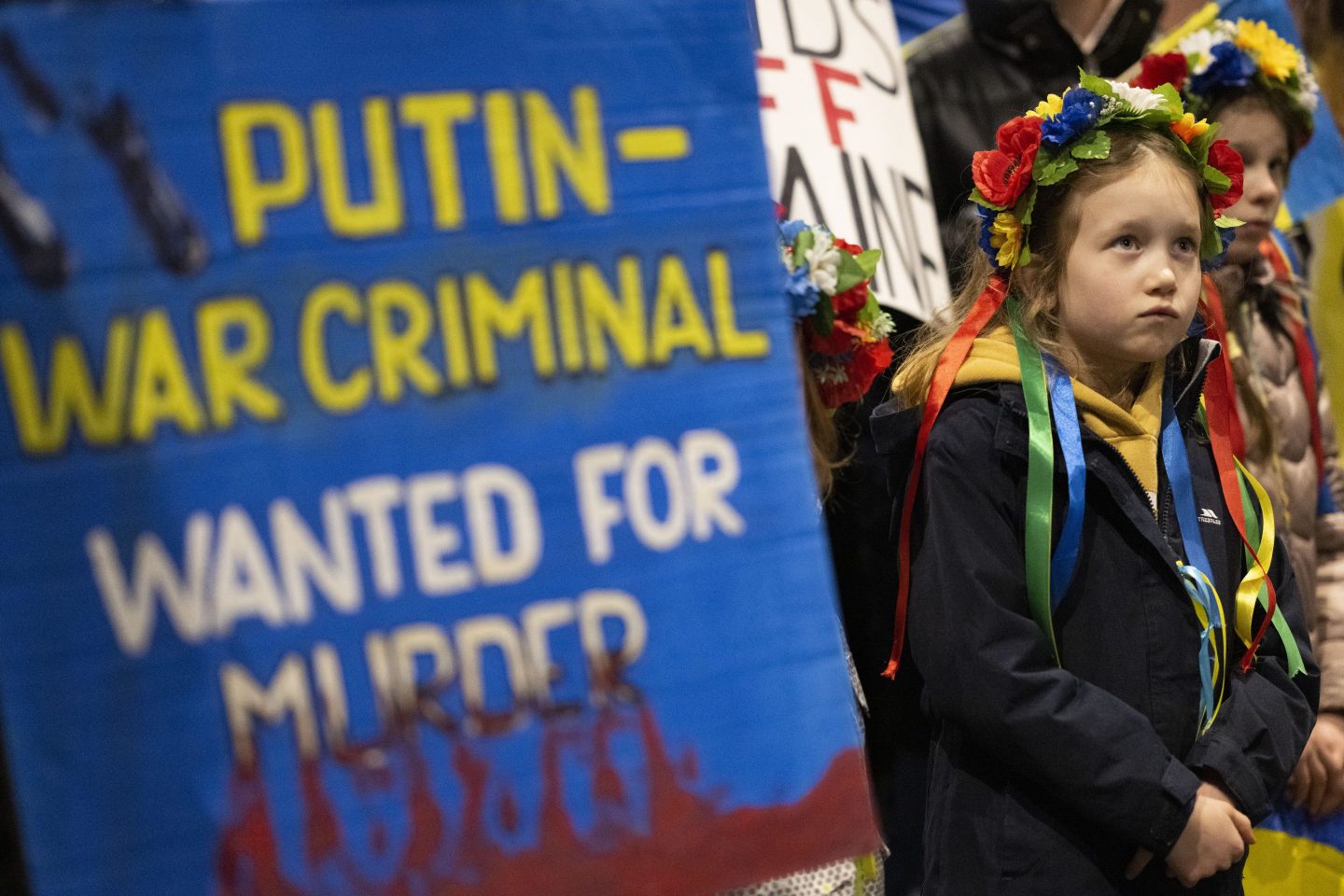 A child looks on near a sign which says Putin war criminal wanted for murder