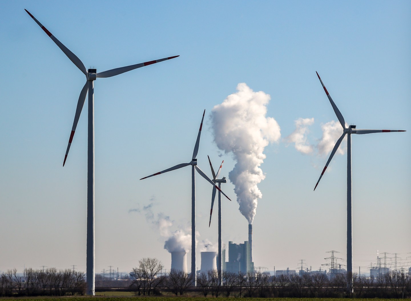 08 March 2022, Saxony-Anhalt, Bad Lauchstädt: The chimney and cooling towers of the Schkopau lignite-fired power plant are steaming behind a wind farm.