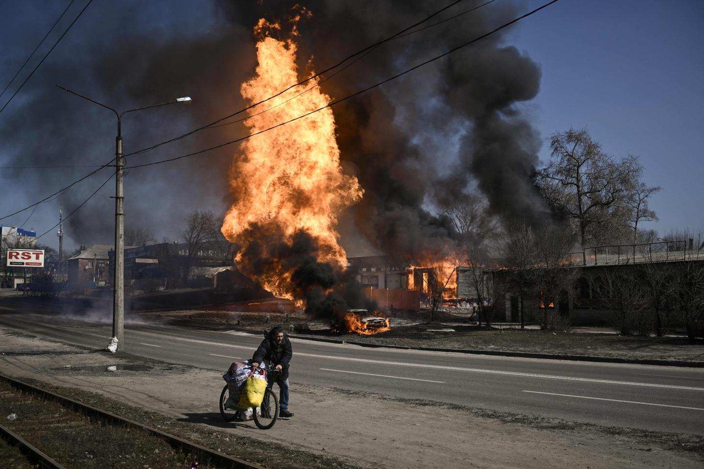 A man flees with his belongings as fire engulfs a vehicle and building following artillery fire on the 30th day on the invasion of the Ukraine by Russian forces in the northeastern city of Kharkiv on March 25, 2022. - Russian strikes targeting a medical facility in Ukraine's second city of Kharkiv on March 25, 2022, killing at least four civilians and wounding several others, Ukrainian officials said. (Photo by Aris Messinis / AFP) (Photo by ARIS MESSINIS/AFP via Getty Images)