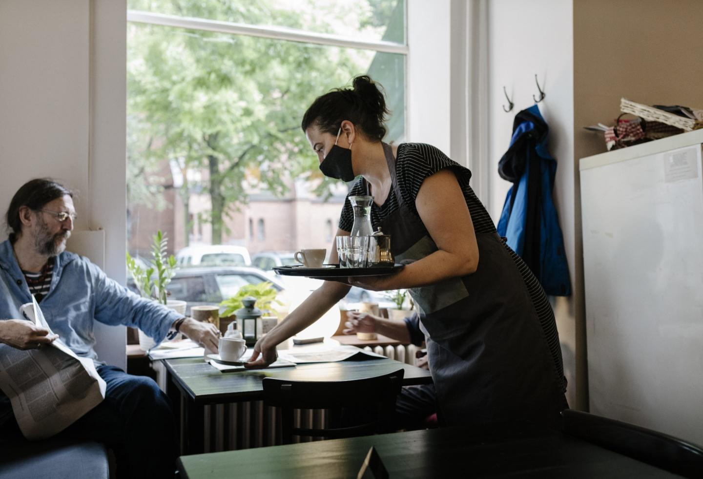 Waitress wearing a face mask clears table of dishes