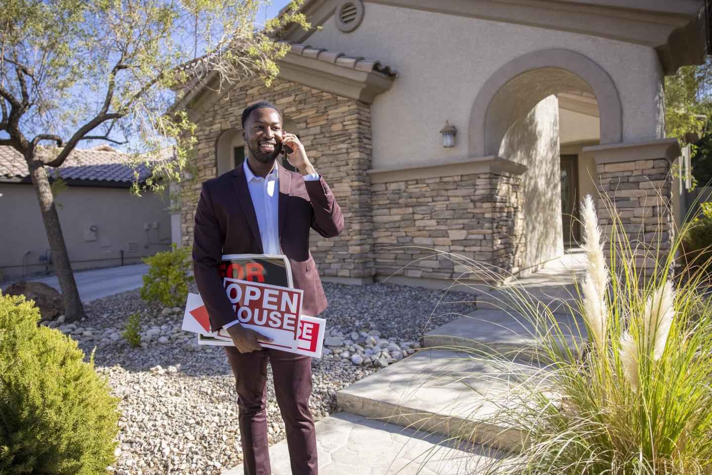 a man on a cell phone holding open house signs stands outside a home.