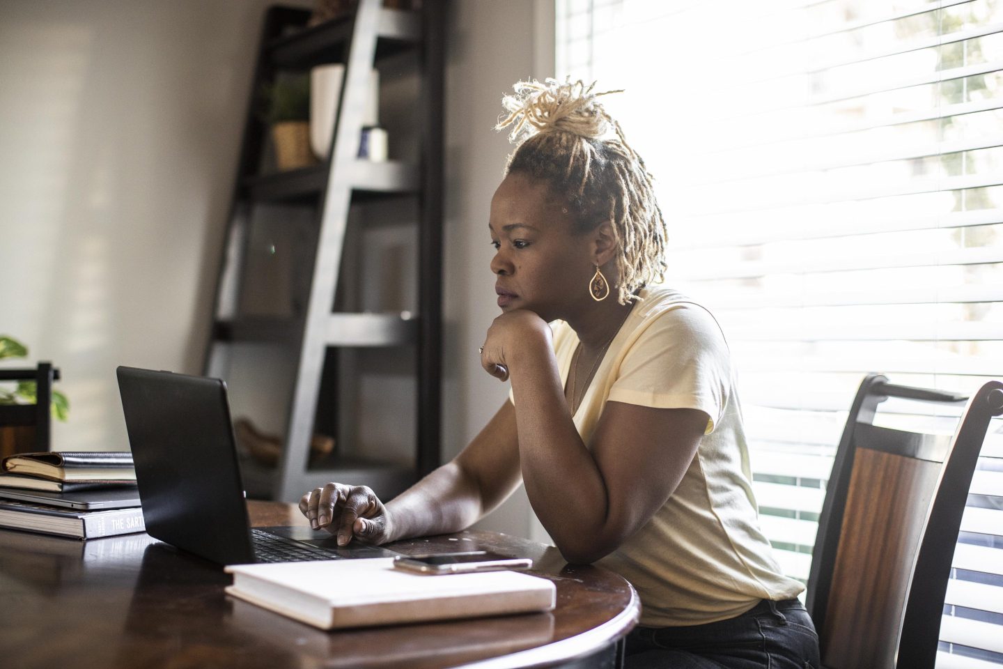 A young woman works on her laptop at her dining room table