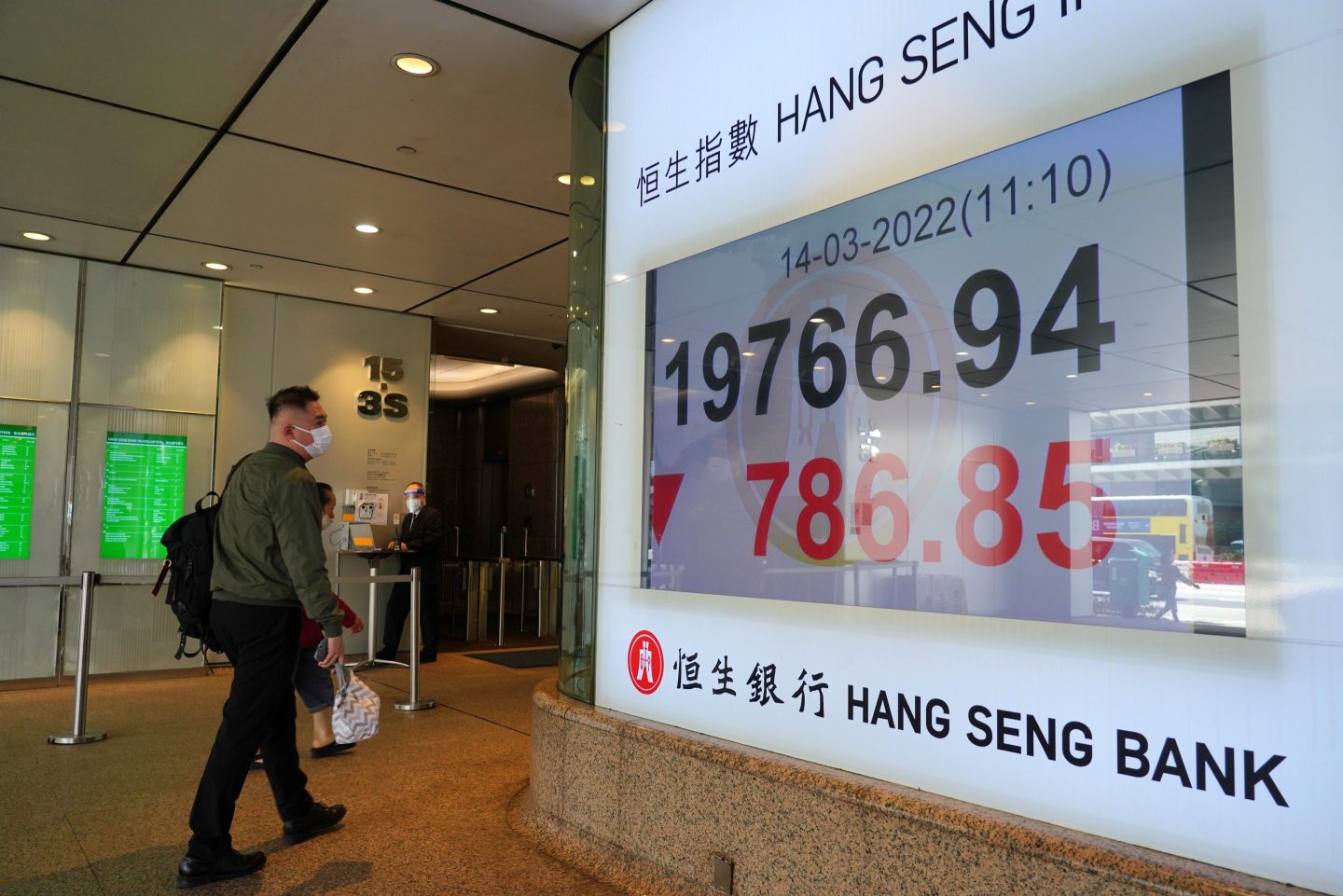 Pedestrian walks by Hang Seng Index sign.