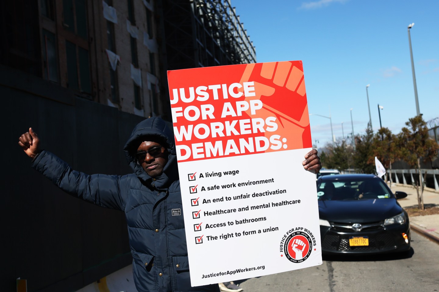 Aziz Bah, an Uber and Lyft driver and organizer of the protest, walks as he carries a sign as he joins other app-based drivers and delivery workers take part in a protest at the former headquarters of Uber.