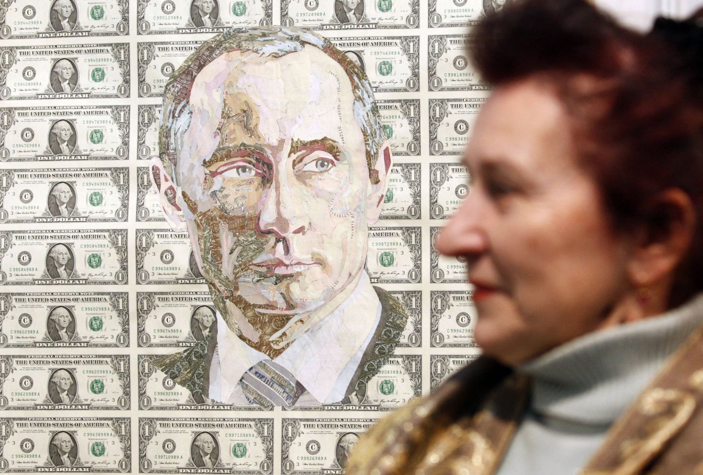 A woman walking by a poster depicting the face of Russian President Vladimir Putin superimposed on U.S. dollar bills.