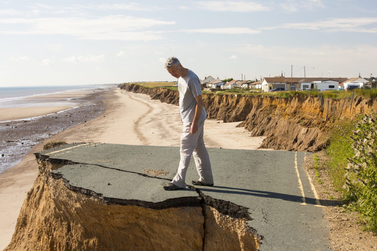 A man stands on an eroded highway near a beach