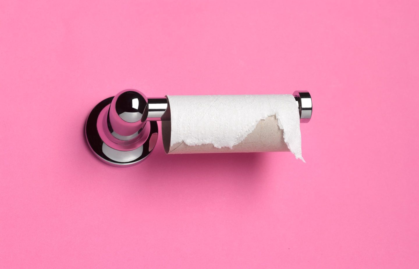 Close up of a toilet roll that has run out on a holder against pink background