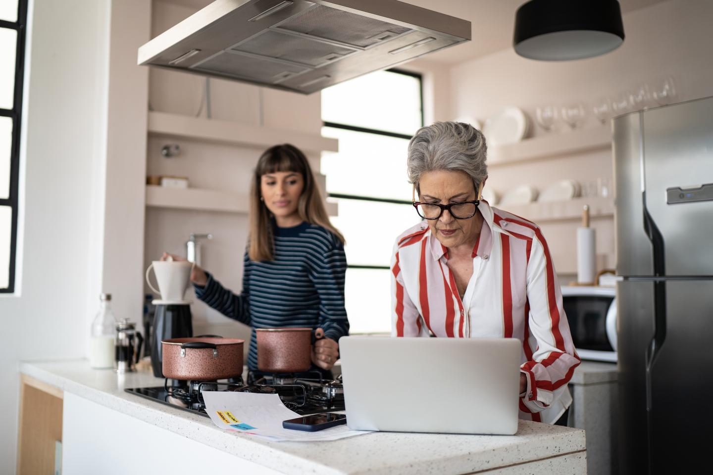 Senior woman working and daughter making coffee at home.