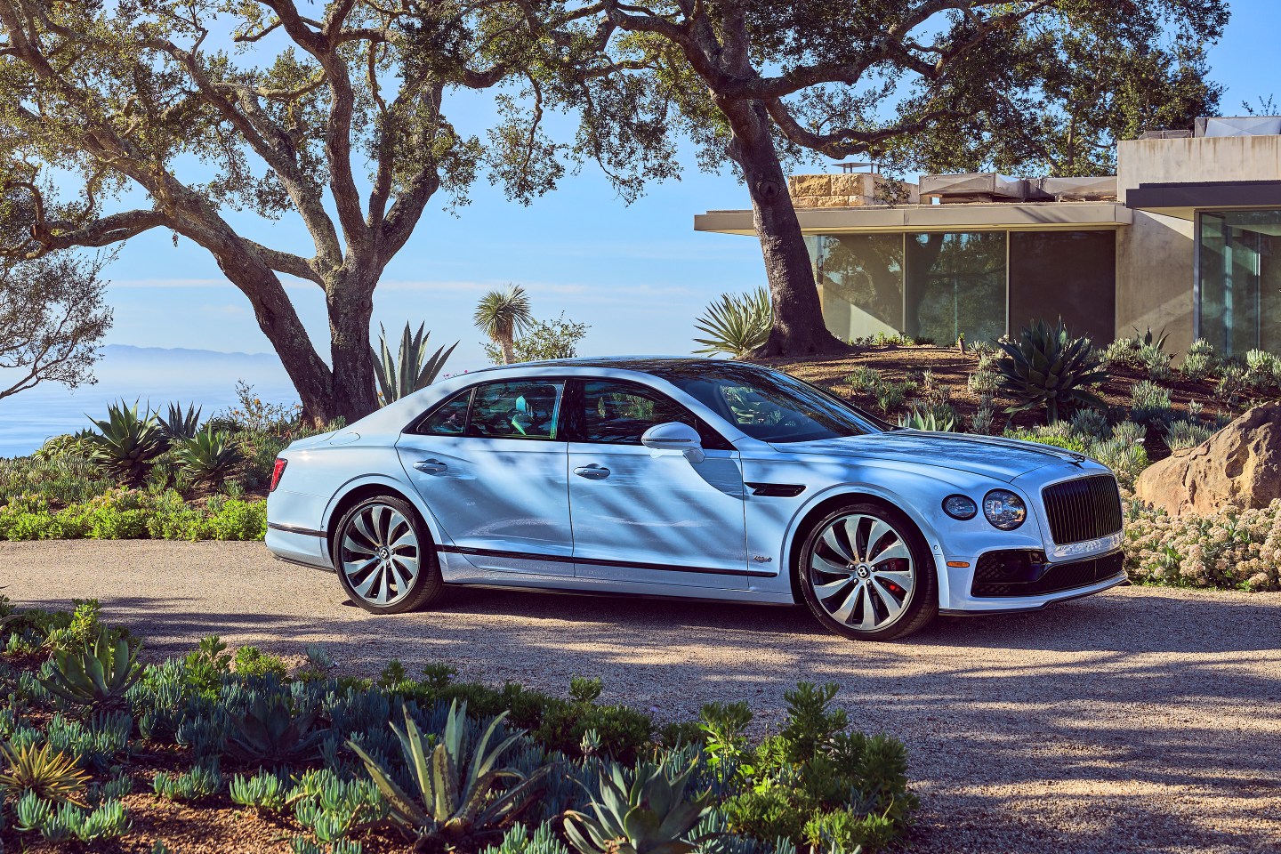 Blue Bentley Flying Spur Hybrid parked outside a house.