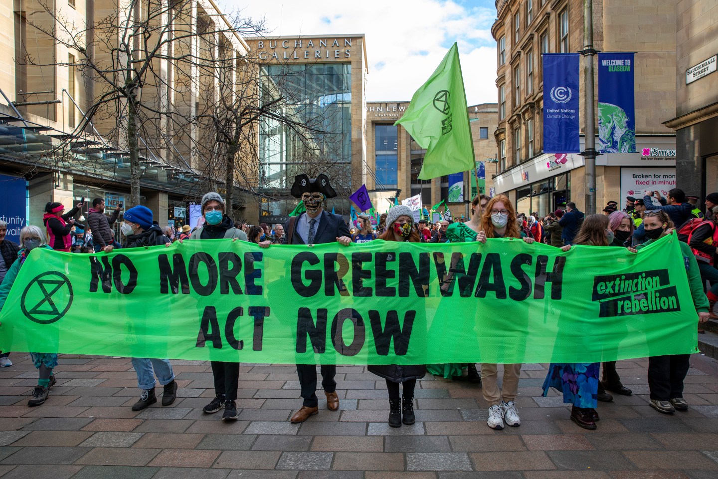 People hold green banner that says "No More Greenwash, Act Now."