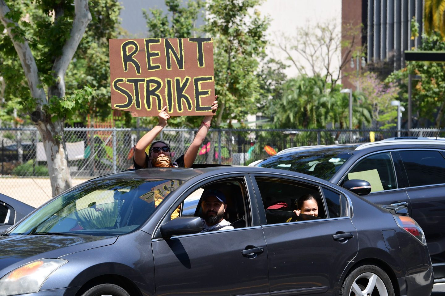 A demonstrator holds up a sign that says "rent strike" out of a car window in California.