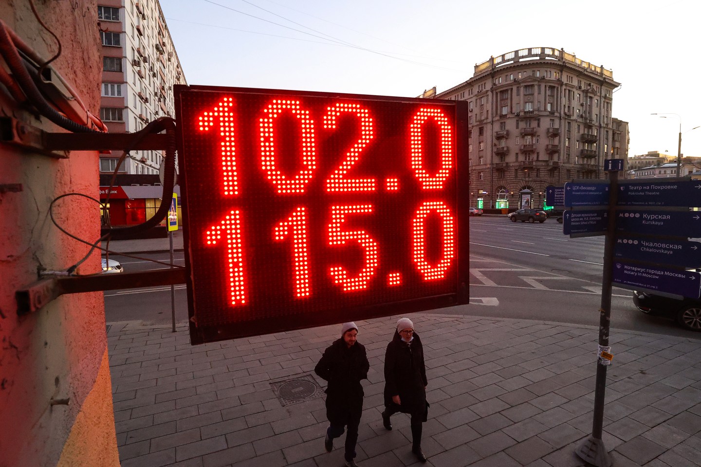 People walk by a digital board showing Russian rouble exchange rates against the euro and the US dollar.