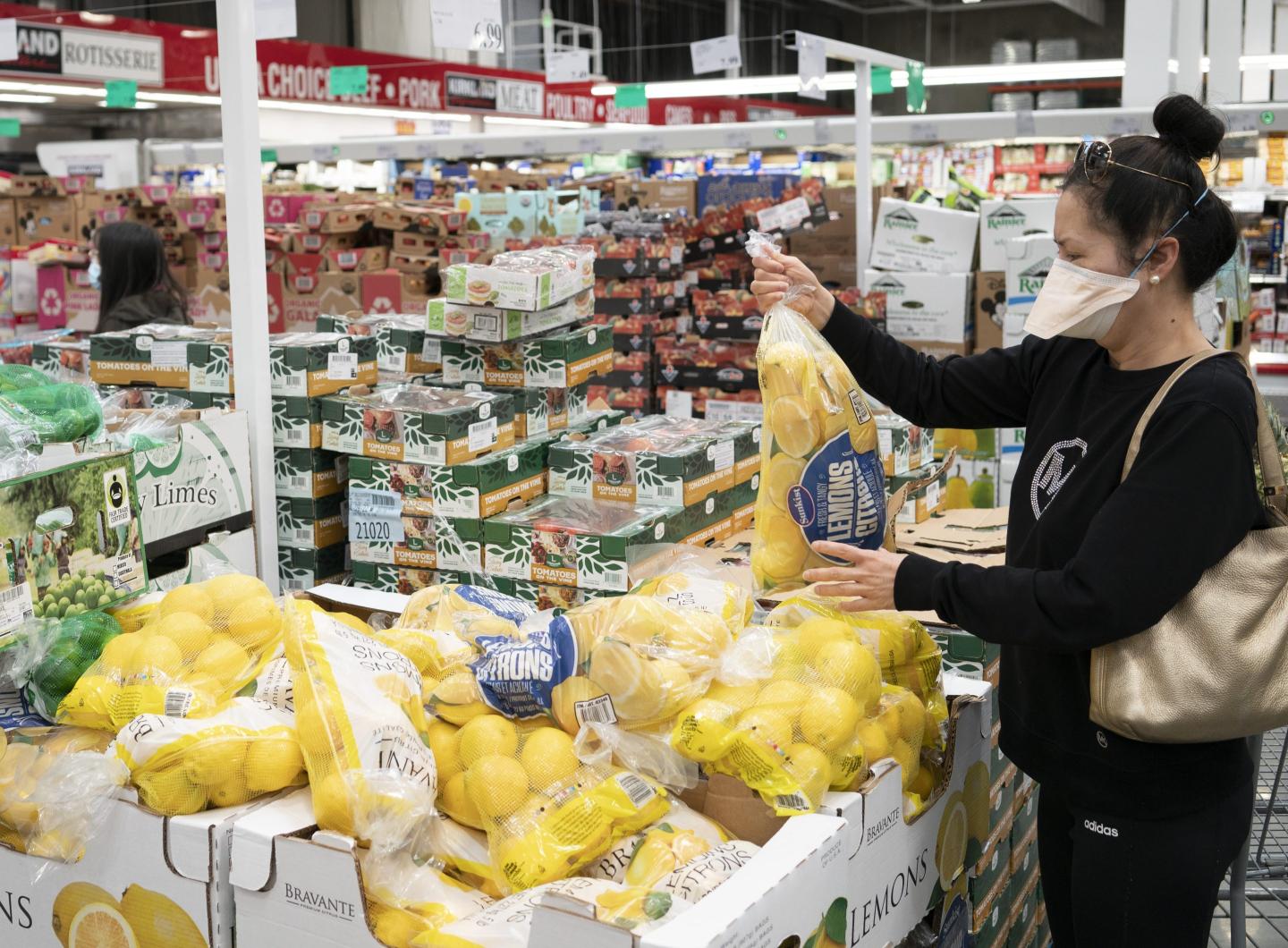 A woman holds a bag of lemons in a Costco.