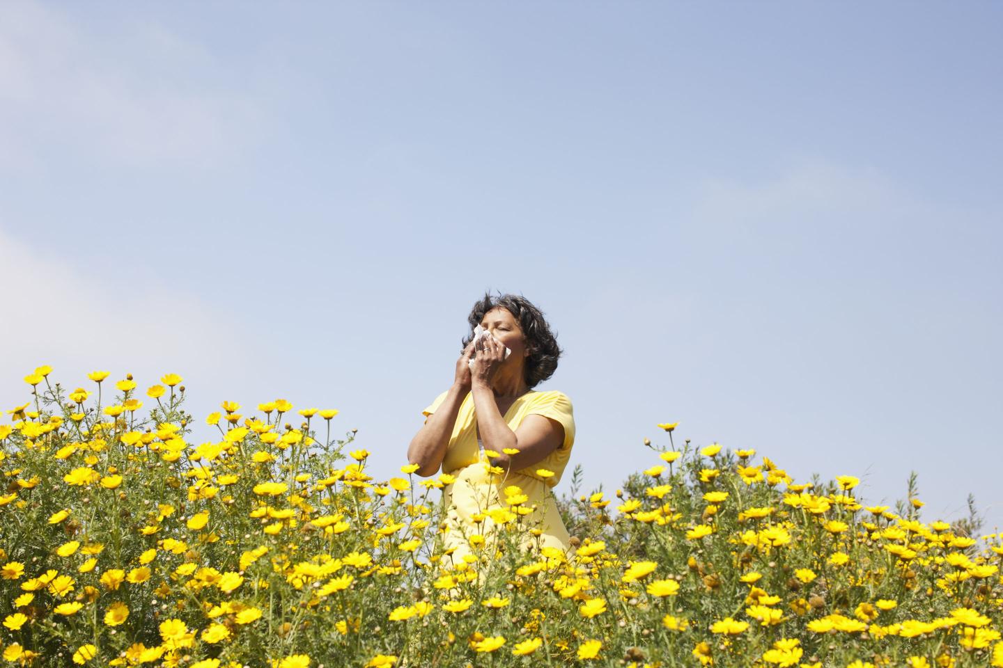 woman in field of flowers sneezing into a tissue