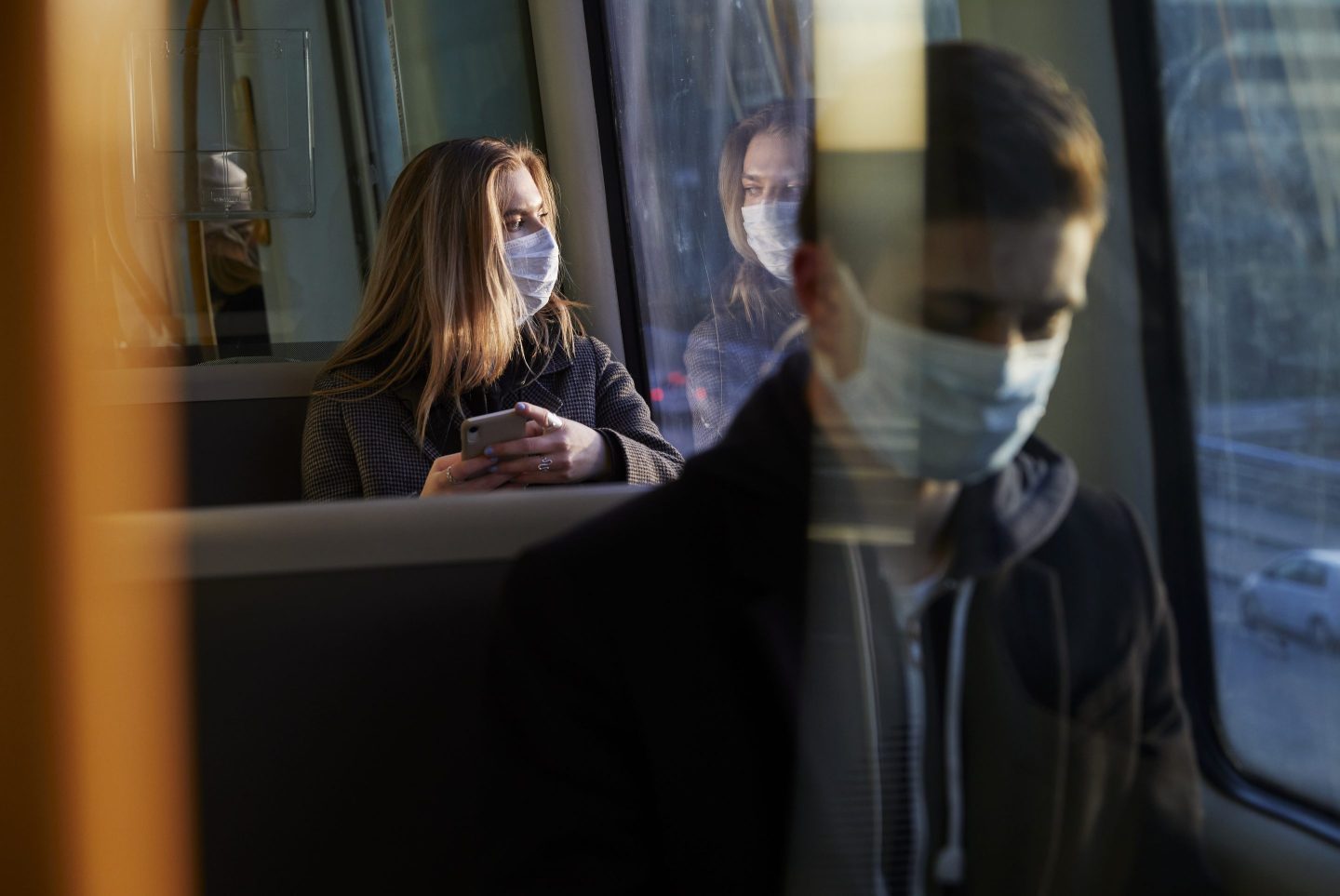 A young woman wearing a mask sits on a train
