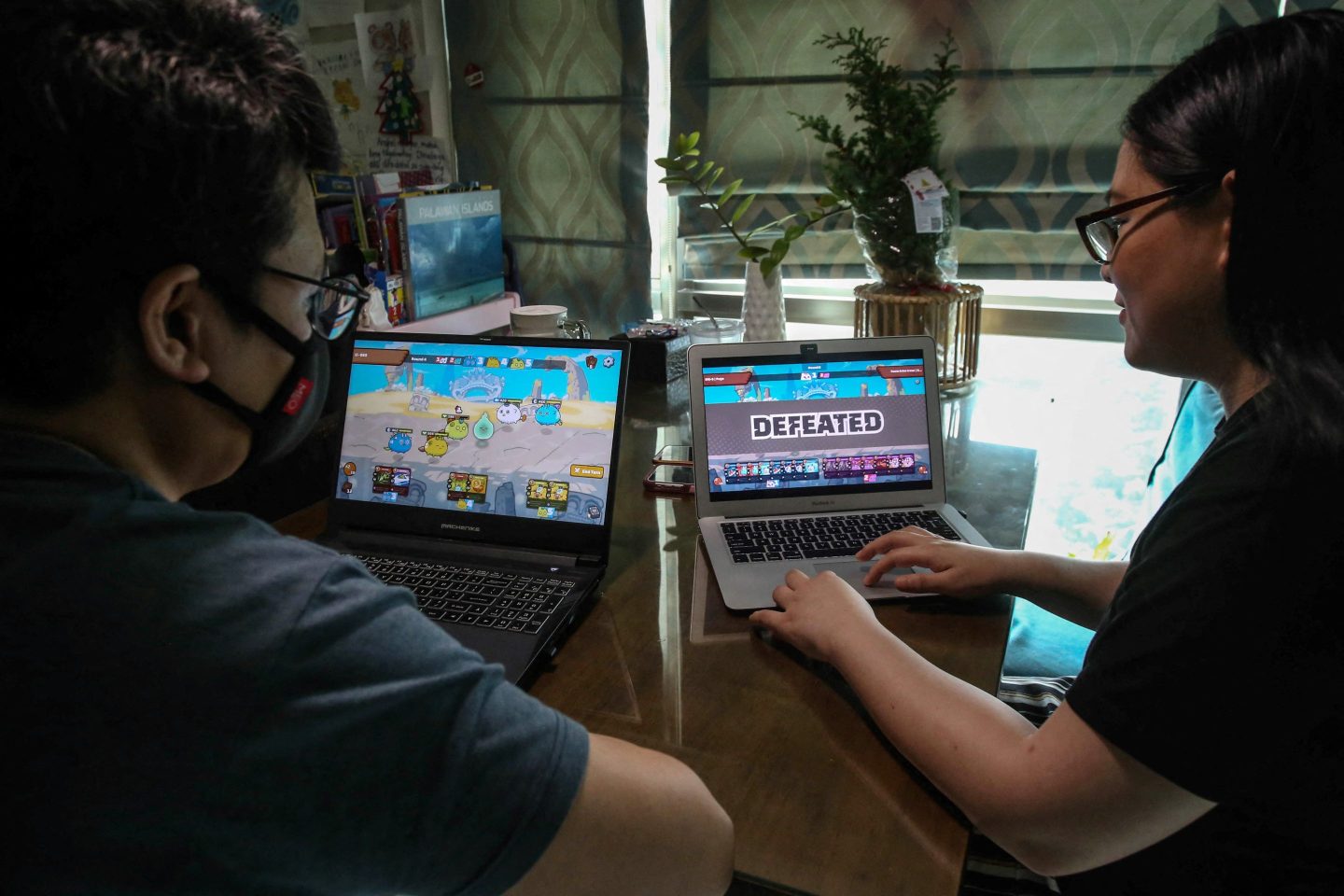 Two people play play-to-earn game Axie Infinity on laptops