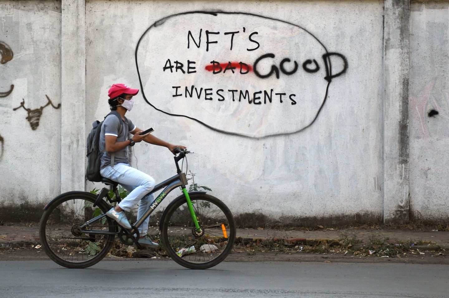 Man on bike rides past graffiti that says 'NFTS are a bad investment' with bad scratched out, replaced by good