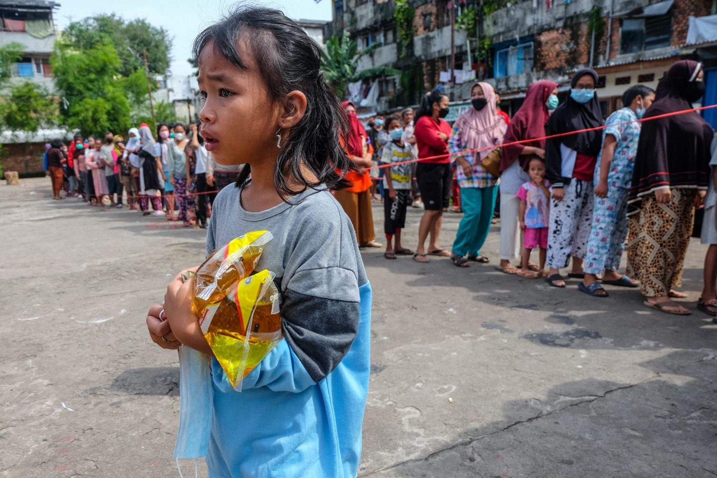 An Indonesian girl carries packs of cooking oil in front of a line of shoppers