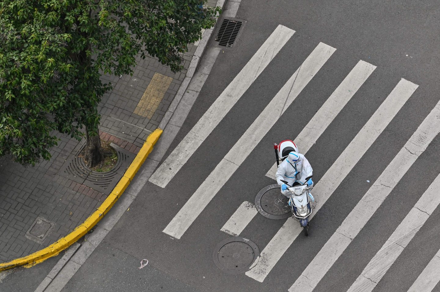 A man in personal protective equipment rides a scooter on an empty street in Shanghai