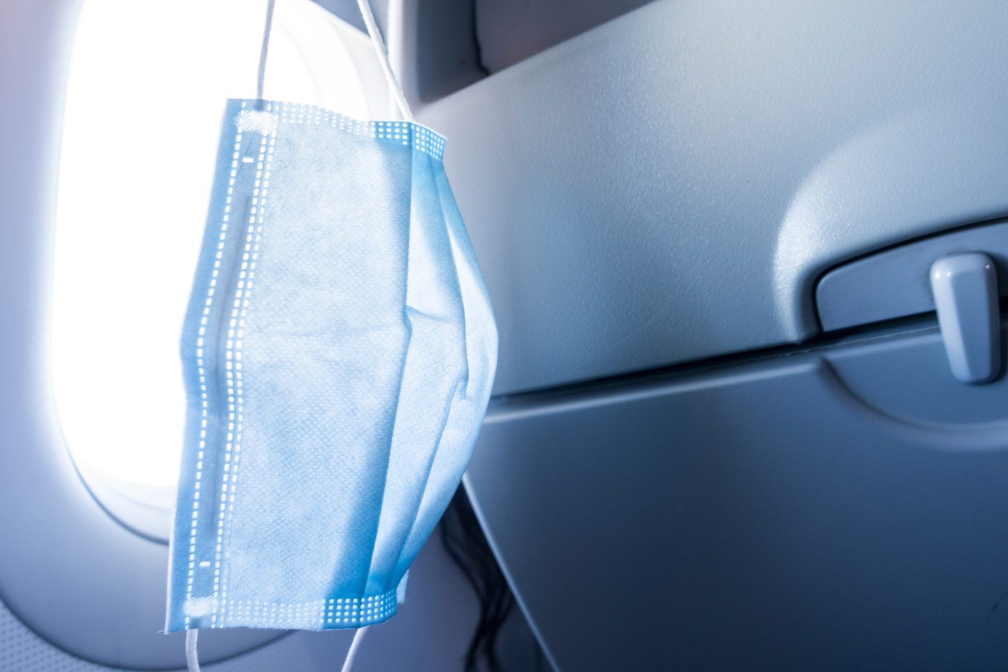 A surgical mask hangs in front of an airplane window