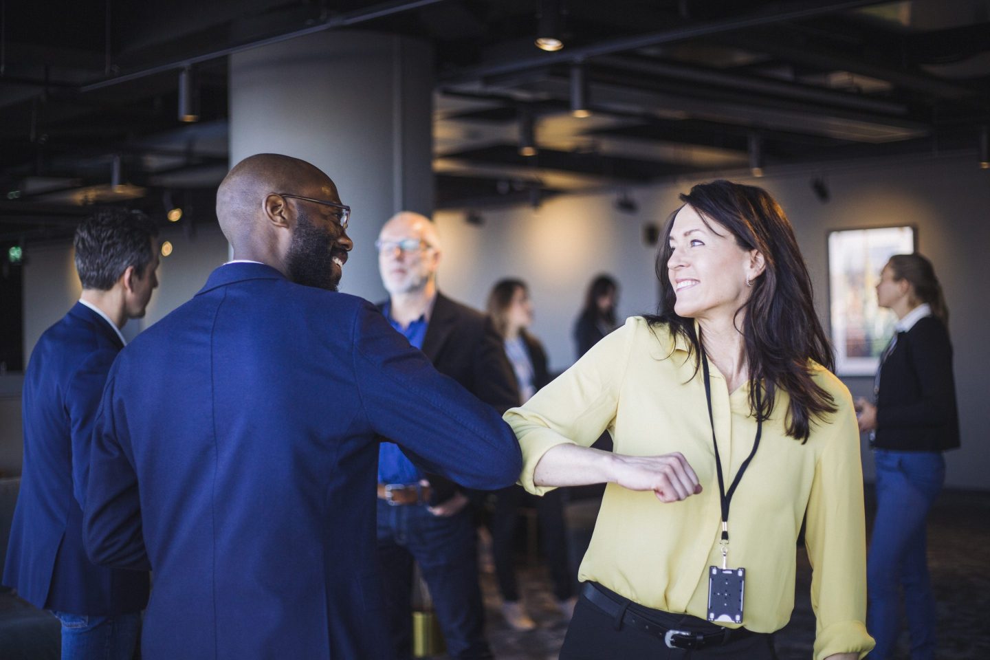 Two colleagues great each other in the office with an elbow tap.
