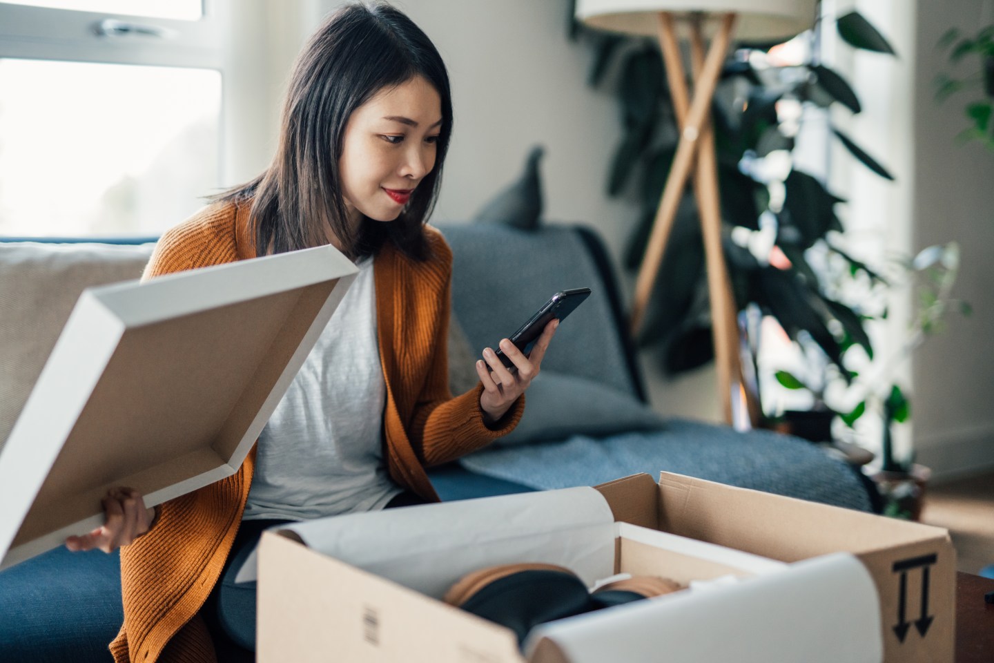 A young woman opens a delivery containing shoes, checks her phone