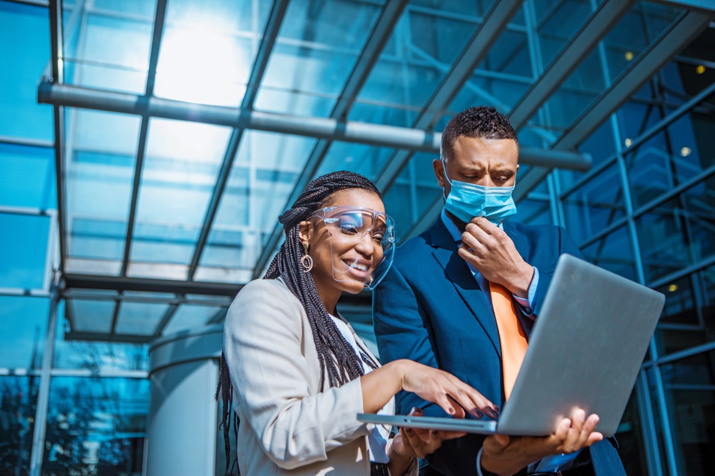 A man and woman wearing protective face masks collaborate at a computer in the office.