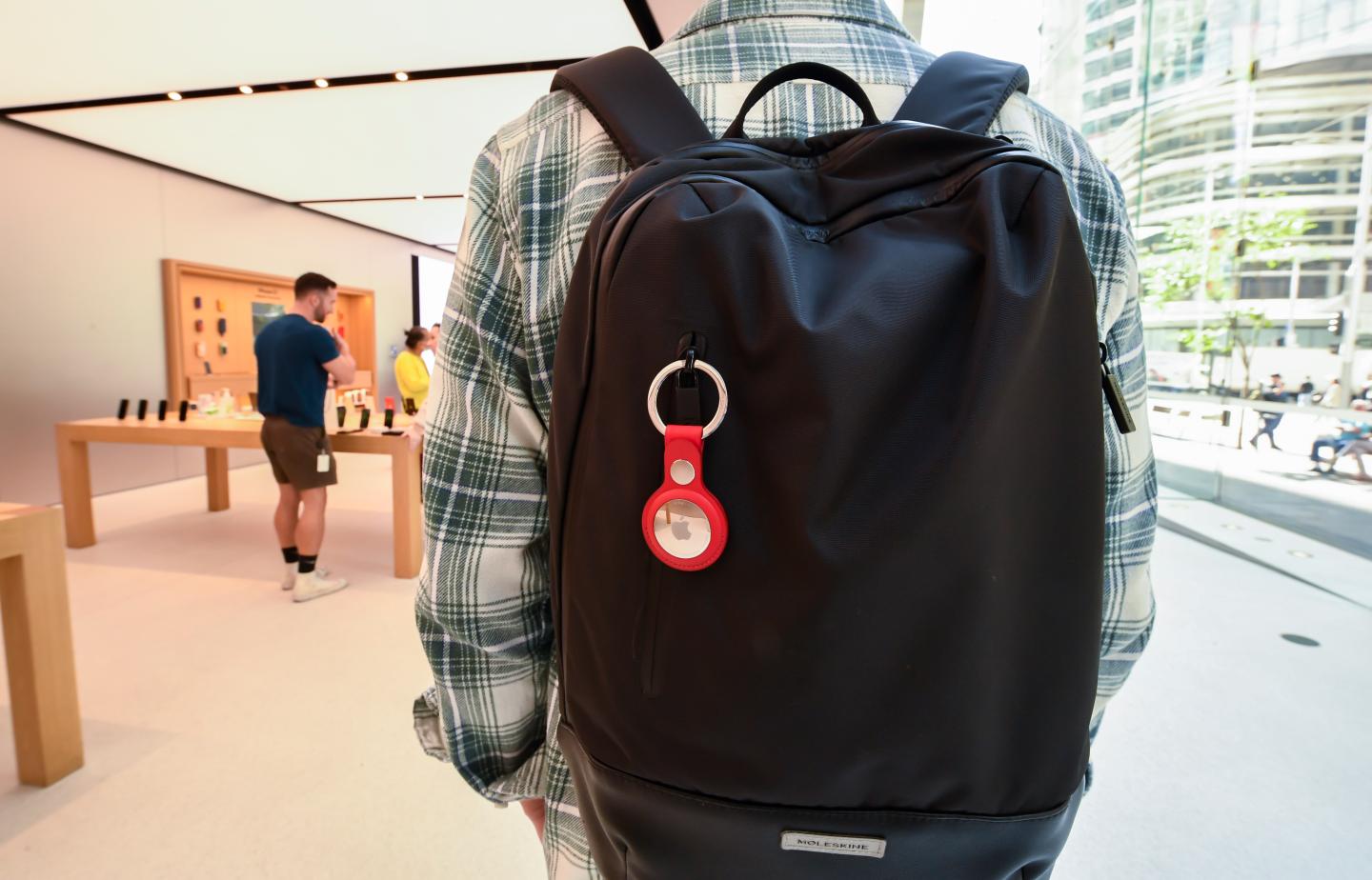 A person wearing a backpack with an attached Apple AirTag and key ring
