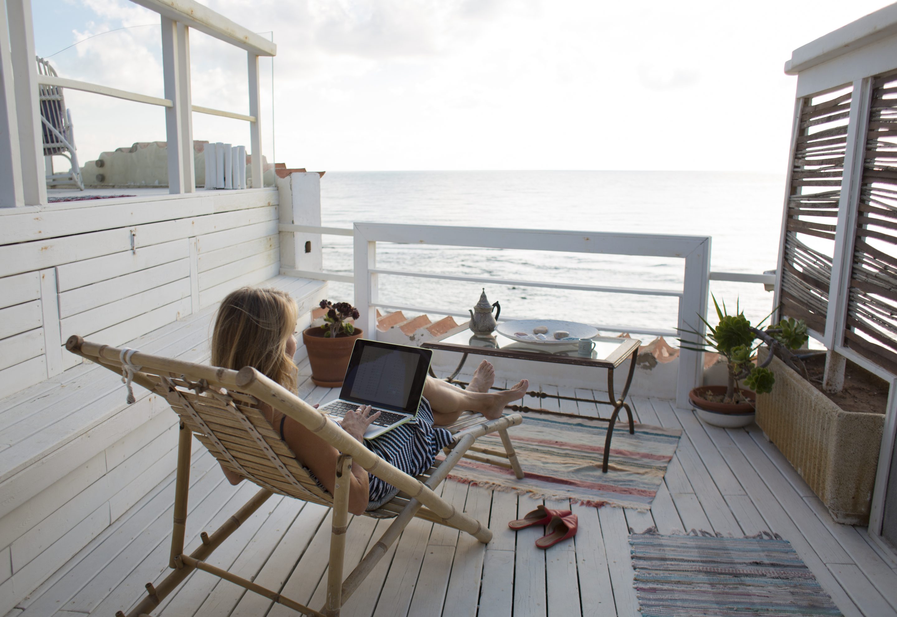 A woman works on a laptop from a seaside deck