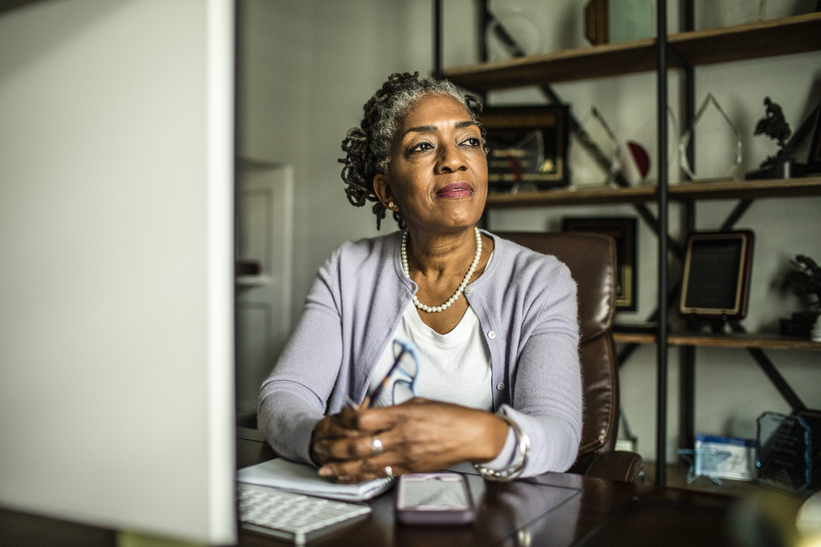 Senior woman sits at desk and gazes into distance