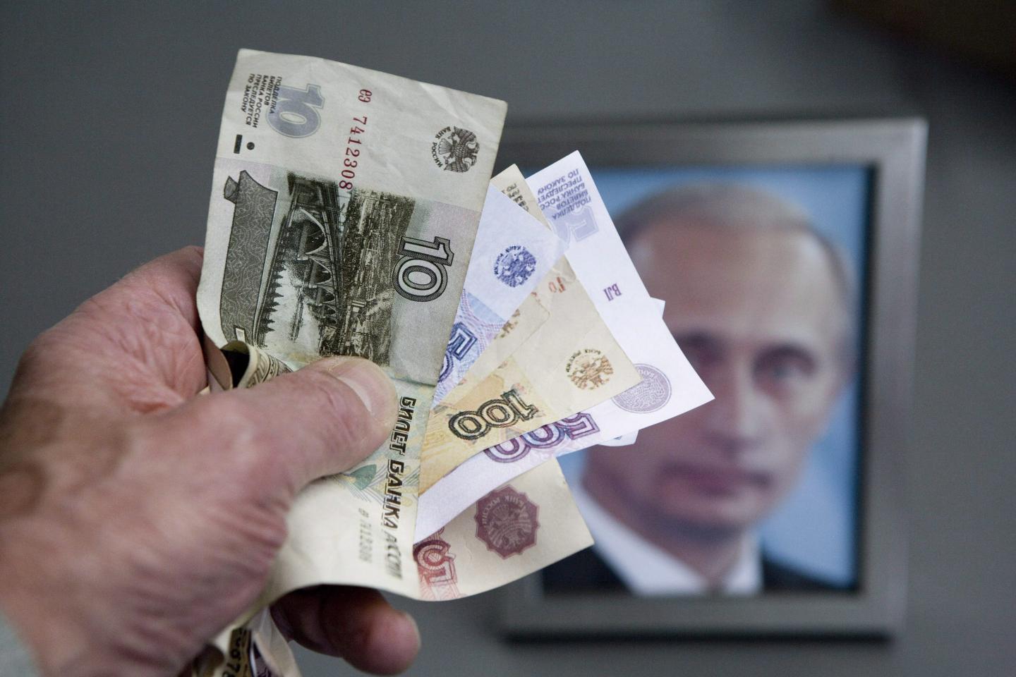 Hand with russian ruble banknotes and a framed Putin photo in the background