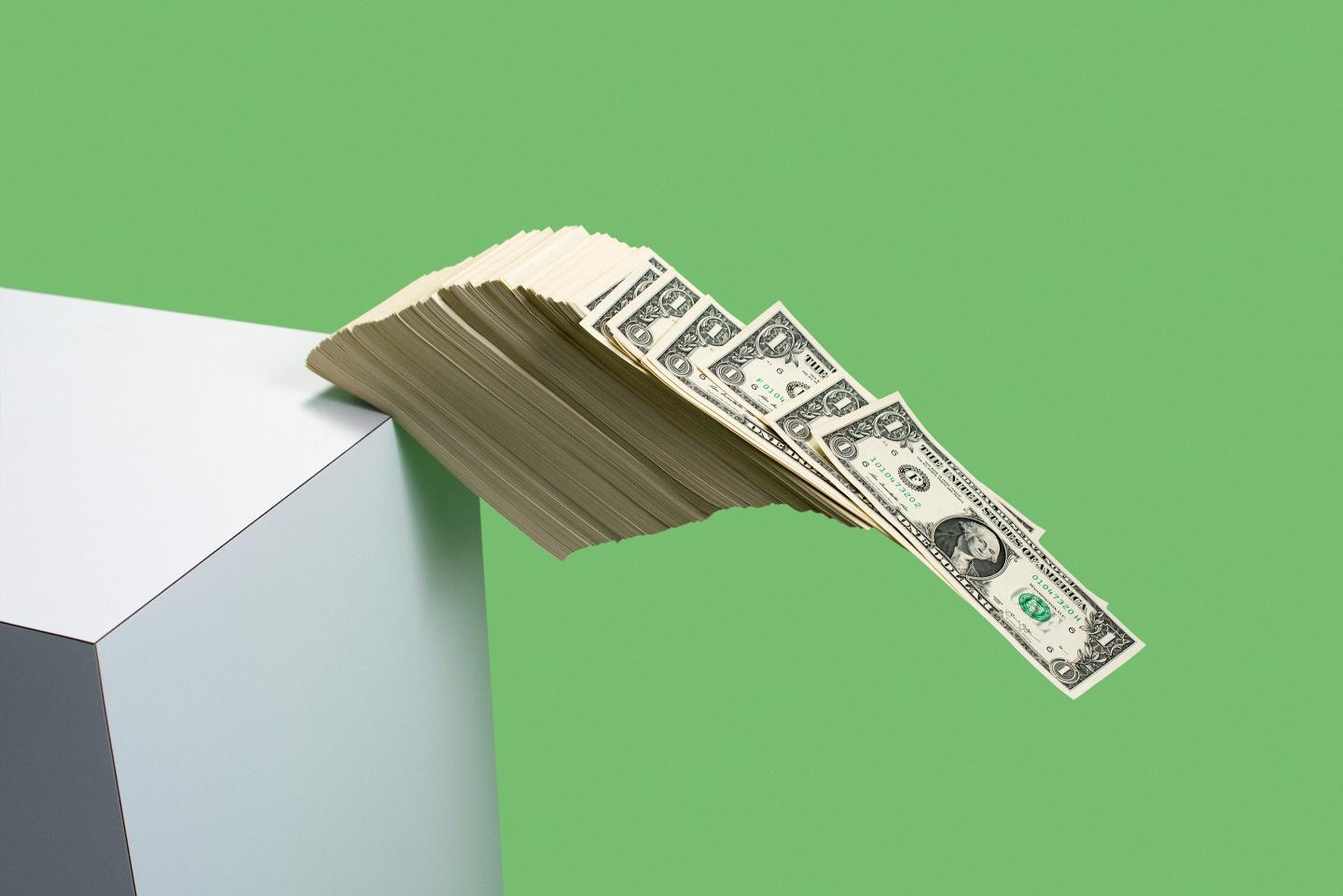 Stack of U.S. $1 bills fall over the edge of a shelf.