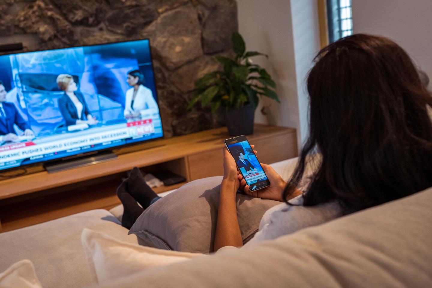 Woman sitting in living room and watching news broadcast